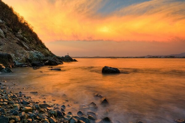 Puesta de sol naranja en la costa rocosa del mar