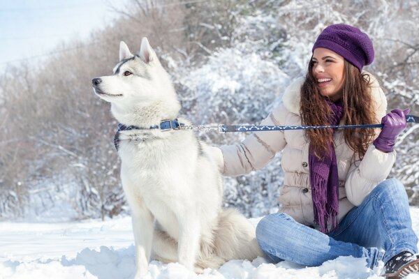 Schönes Mädchen sitzt mit einem Husky im Schnee