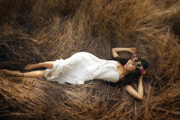 一个穿着白色连衣裙的女孩躺在干燥的草地上