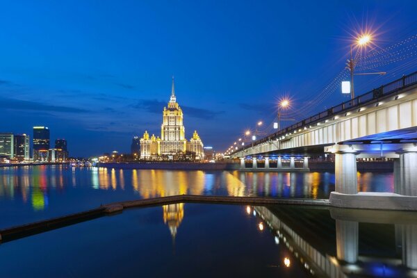 Architecture of the night city with a long bridge over the water surface