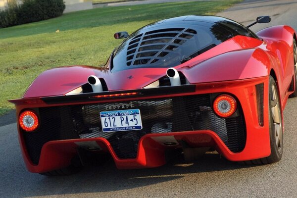 Auto sportiva rossa sulla strada asfaltata accanto al prato verde