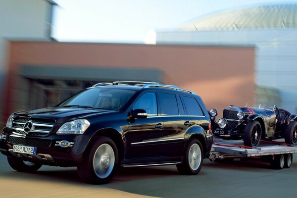 Mercedes preto com um reboque em que há um carro retrô