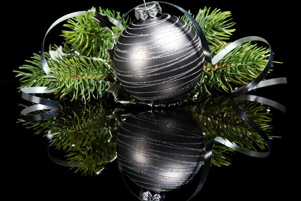 Bola de plata con ramas de árbol de Navidad verde en espejo negro