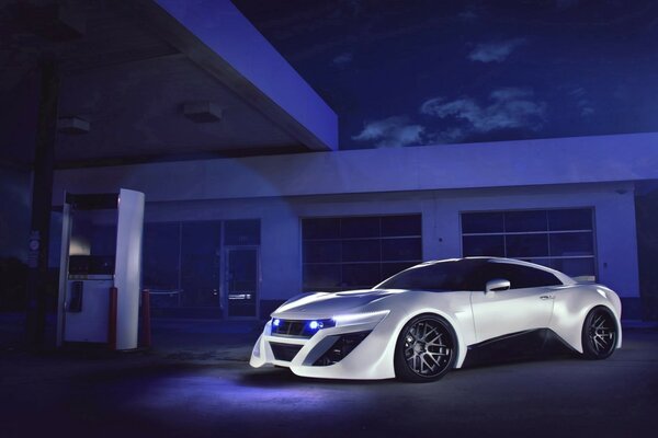 A white sports car on the background of a purple gas station