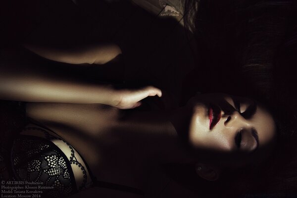 Девушка лежит в темноте с красными губами