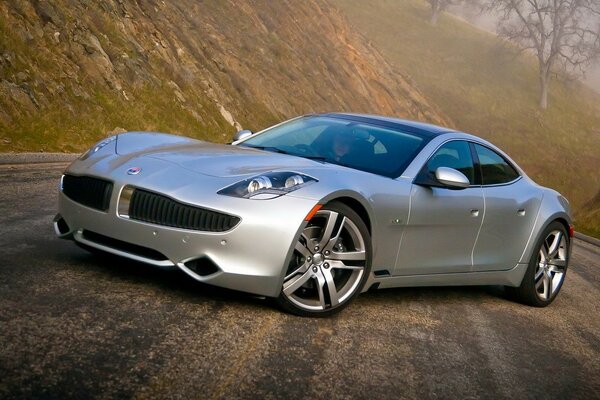 A silver sports car stands on the road among the green hills