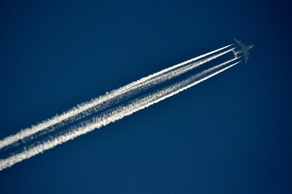 Ein Flugzeug in hellblauem Himmel fliegt und hinterlässt zwei weiße Spuren