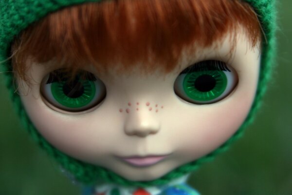 A doll in a knitted green hat with huge green eyes