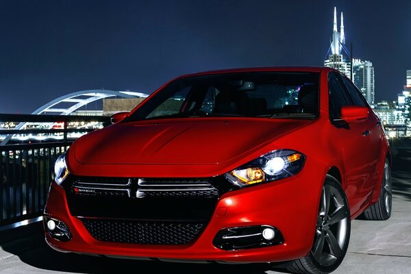 Un auto sportiva rossa si trova sullo sfondo di una città notturna nelle luci