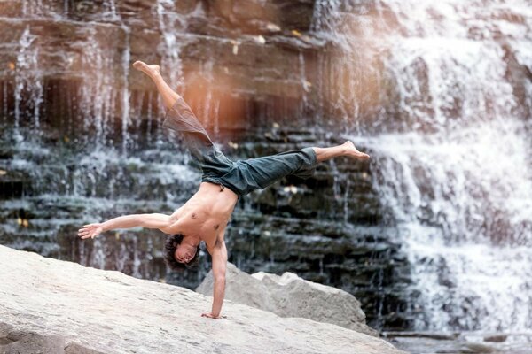 A man performs a one-handed stand near a waterfall