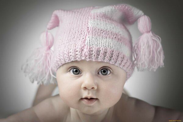 Chubby baby in a pink cap with tassels