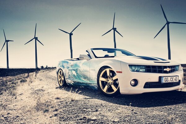 A white car drives past wind turbines