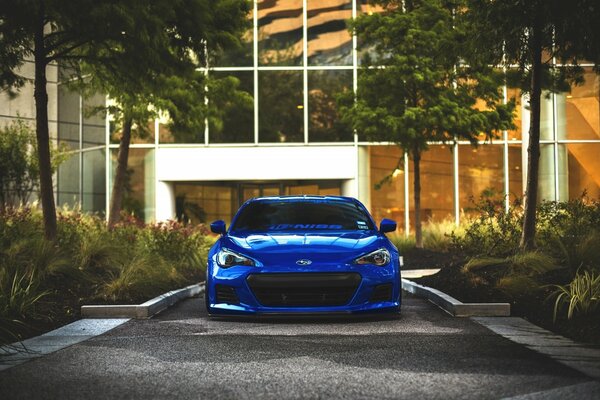 Gorgeous blue car on the sidewalk near a big house