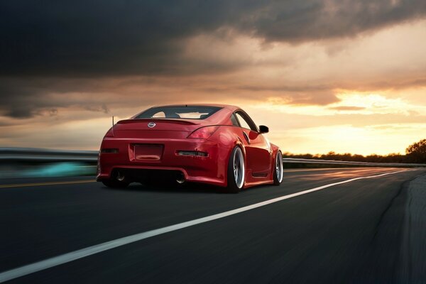 A red car on the road against the background of sunset