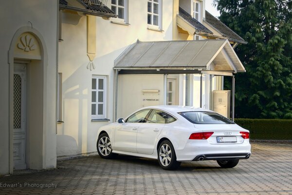 Audi blanco cerca de una hermosa casa arquitectónica