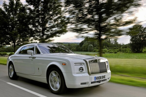 A white luxury car is driving on the road