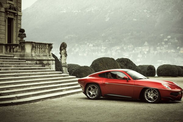 A red car near a mansion in the city at the foot of the mountain