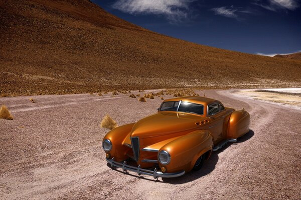 A yellow car is driving in the middle of the desert