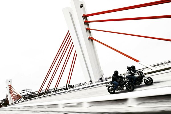 Three bikers are racing across the bridge