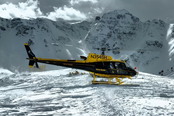 Yellow-black helicopter in the snow on the background of mountains