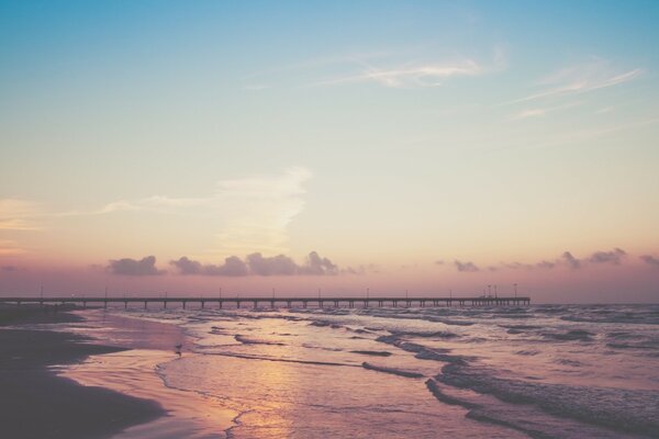 A bridge in the distance and waves against a pink-blue sky