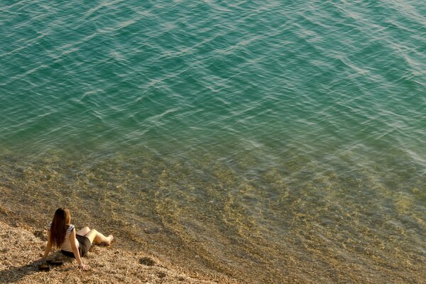 Côte et fille assise sur le rivage