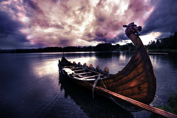 Un bateau semblable à un Drakkar Viking amarré sur un lac au coucher du soleil