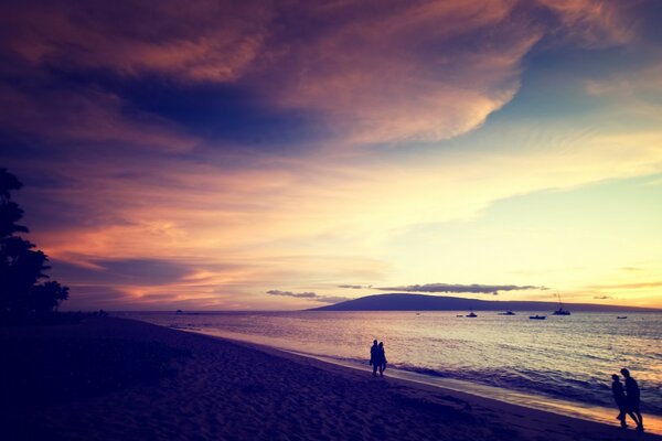 Paare, die bei Sonnenuntergang am Strand spazieren gehen