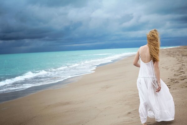 Красивая девушка в белом платье идёт по пляжу