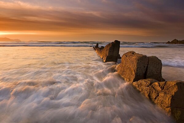 The ocean crashes into big rocks at sunset