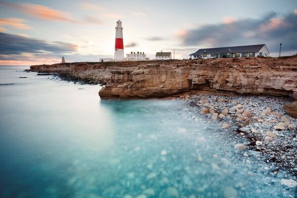 O oceano lava uma praia rochosa, um farol é visível à distância