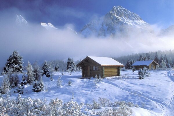 A hut in a winter forest against the background of mountains