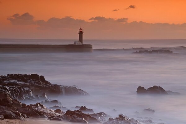 Lighthouse in the sea on the background of sunset