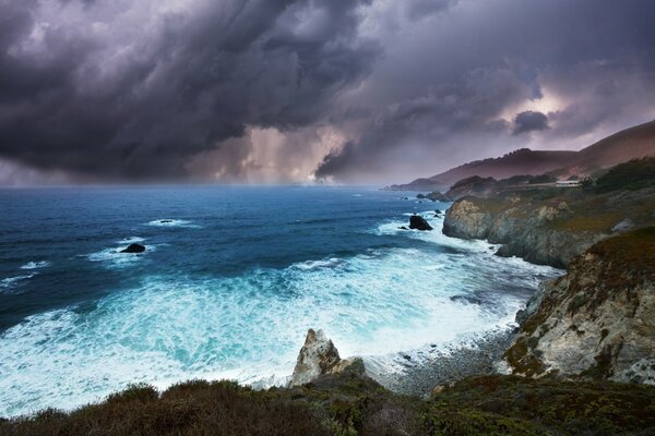 Seawater rages along the rocky shores under a cloudy sky