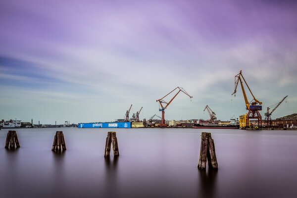 Industrielle Kräne und Frachtcontainer im Hafen vor dem Hintergrund des bewölkten Himmels und des ruhigen Meeres