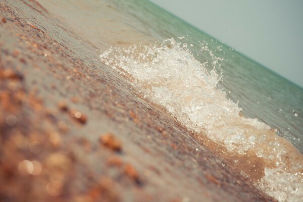 Azure wave plays with pebbles on the shore