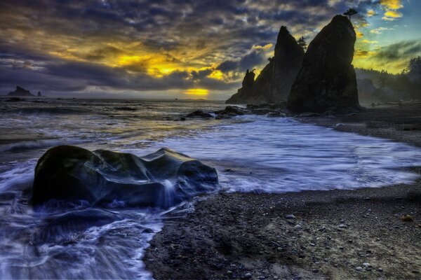 Waves on a rocky shore at sunset with a cloudy sky