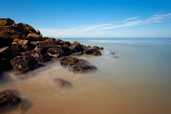 Água do mar calma na costa rochosa sob o céu azul