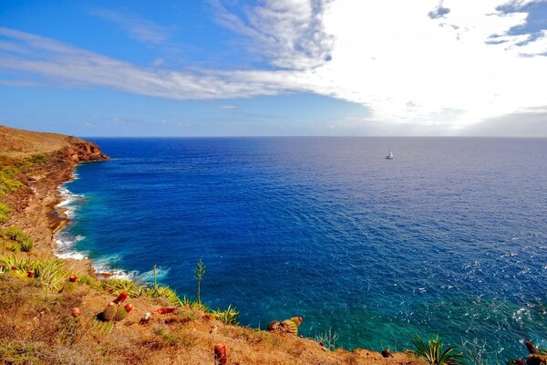 A lonely boat on the blue surface of the sea under white clouds