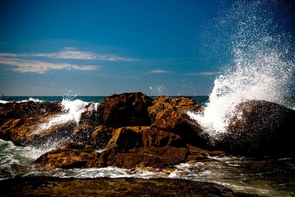 Waves crashing against rocks against a blue sky background