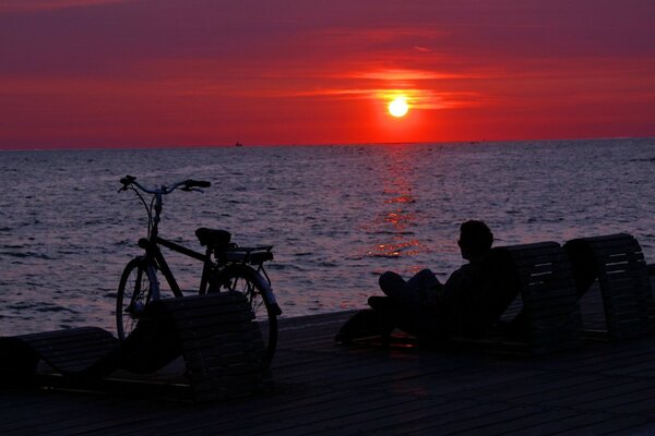 Человек на закате у моря с велосипедом