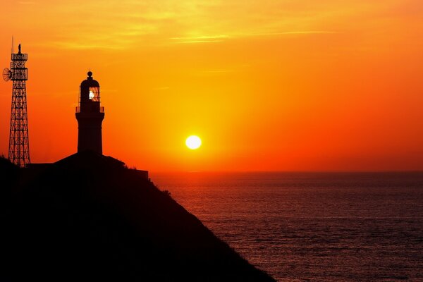 Faro en una roca sobre el mar en la luz roja del sol que se va