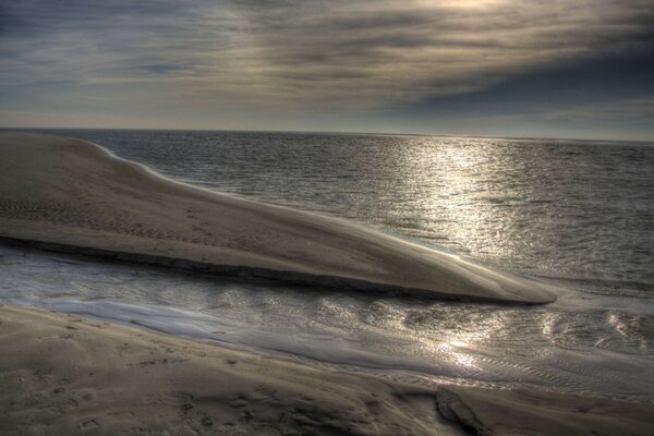 Ein Wüstensandstrand, der vom Meer unter bewölktem Himmel gewaschen wird