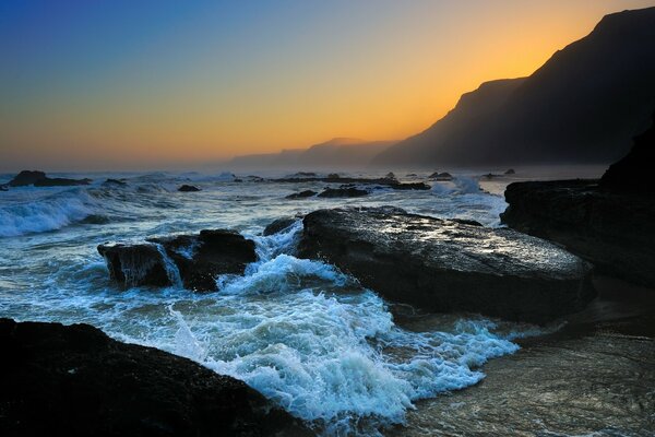 Olas que golpean las piedras en el fondo de la puesta de sol