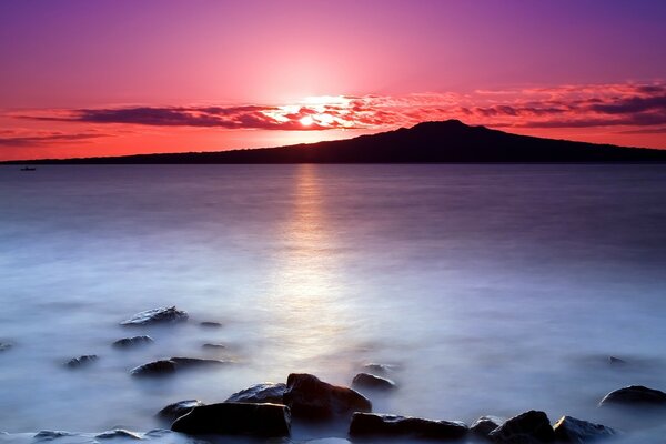 Brillante puesta de sol en el mar y piedras en el agua