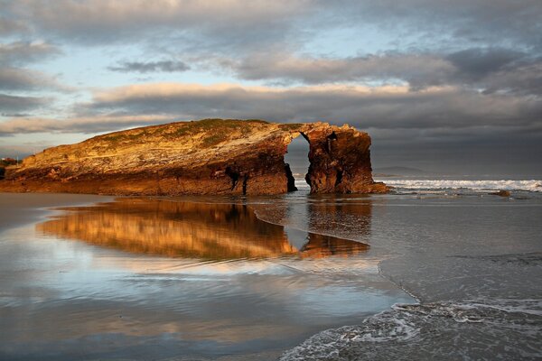 Ein Felsen, der bei Sonnenuntergang von den Wellen des Ozeans umhüllt ist