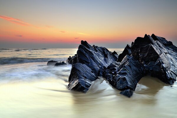 Waves cut through the black rocks