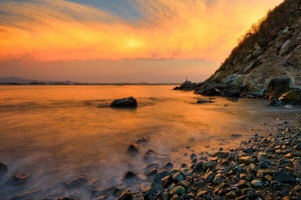 Landschaft von Bergen , Meer , Steinen und feurigem Sonnenuntergang