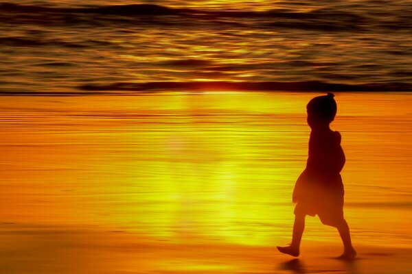 Kind, das bei Sonnenuntergang am Strand spazieren geht