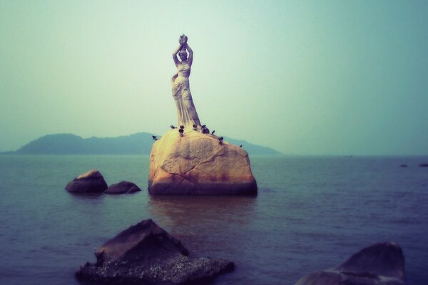 A girl stands on a rock in the sea